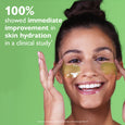 Woman wearing golden gel eye patches under eyes against green background.
