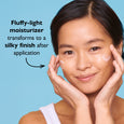 Woman applying light cream moisturizer to cheeks against blue background.