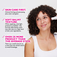 White cylindrical stick product being applied to cheek of person with curly dark hair and gold hoop earrings.