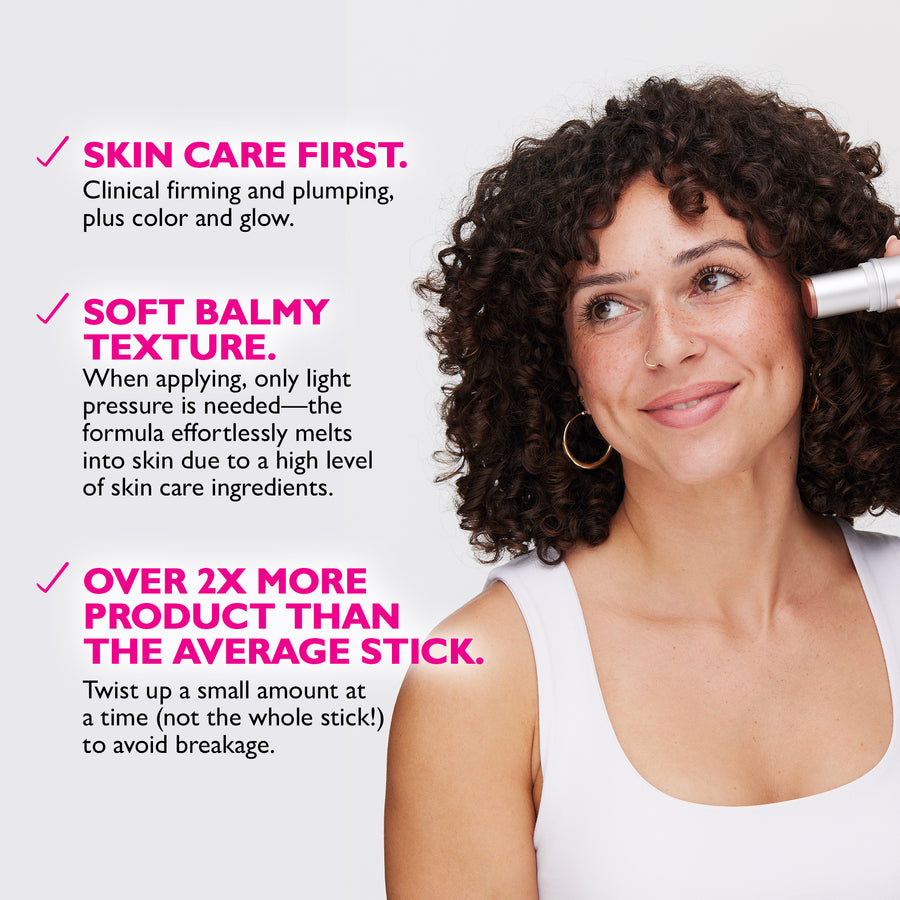 White cylindrical stick product being applied to cheek of person with curly dark hair and gold hoop earrings.