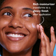 Person applying cream to cheek, showing moisturized skin with luminous finish.