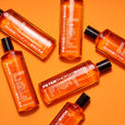 Multiple bottles of Peter Thomas Roth Anti-Aging Cleansing Gel in orange liquid form with black caps on yellow background.