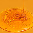 Clear orange gel with visible exfoliating particles in a petri dish with liquid being poured in.