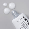 White tube of acne treatment gel with clear applicator top and product information label, displayed with three white gel drop