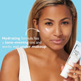 Woman holding white SPF 45 moisturizer tube with sheer tint, displaying product on face against blue background.
