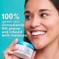 Woman with dark hair smiling while holding white and blue moisturizer jar against turquoise background.