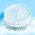 White jar containing light blue gel eye cream with applicator brush against blue sky background.