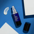 Dark purple bottle with silver pump dispenser, black cap, and white cream swatch on blue background.