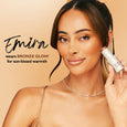 Woman holding white cylindrical stick product with bronze-toned makeup applied to face and shoulders.