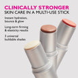 Three white cylindrical stick products with cream, bronze, and pink-toned tops displayed against gray background.