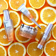 Three skincare tubes and one jar with white and silver packaging displayed on sliced oranges.