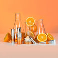 White and orange skincare products arranged with fresh oranges and glass bottles on peach background.